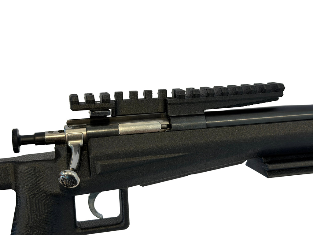 Close-up of a black rifle with a scope rail on a white surface